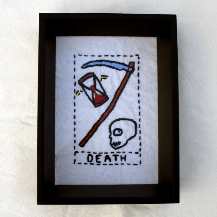 an embroidered tarot card featuring a skull, a scythe, and a flying hourglass