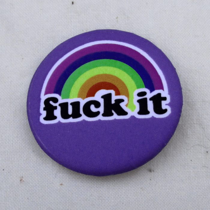 A blue pinback button with a rainbow and the words "fuck it" printed on it