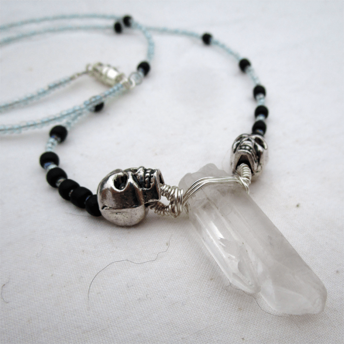 a necklace with a wire-wrapped quartz point pendant, flanked with skulls, strung with glass beads