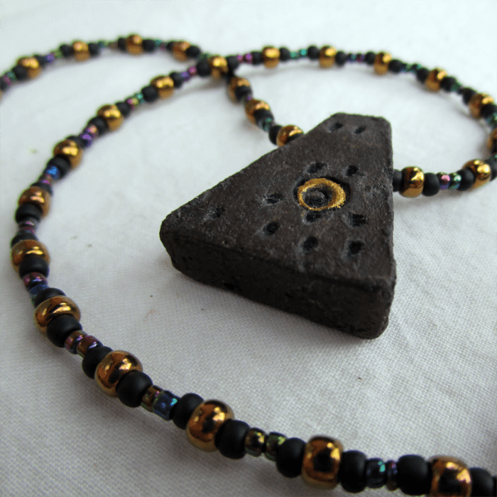 a necklace with a nearly triangular painted ceramic pendant on a strand of glass beads