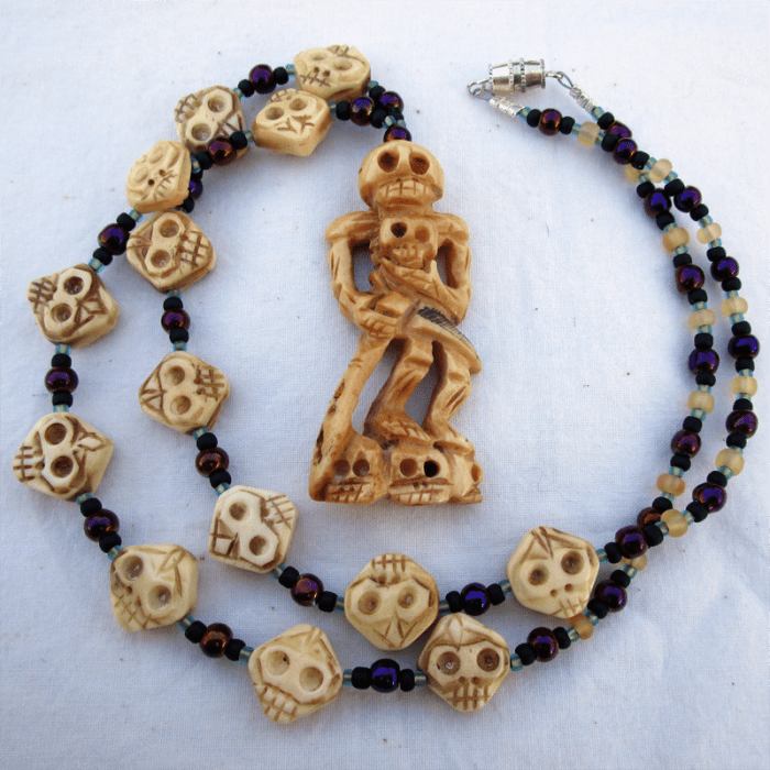 a necklace featuring multiple bone skull beads, glass beads, and a large bone skeleton pendant