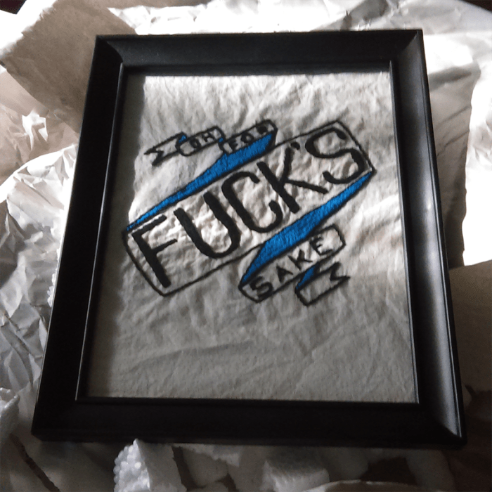 a framed embroidery project of a banner with blue backing that reads 'oh for fuck's sake'