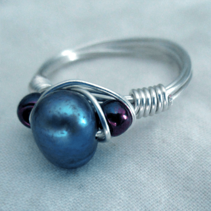a wire wrapped ring with a dark freshwater pearl and iridescent blue/purple glass beads